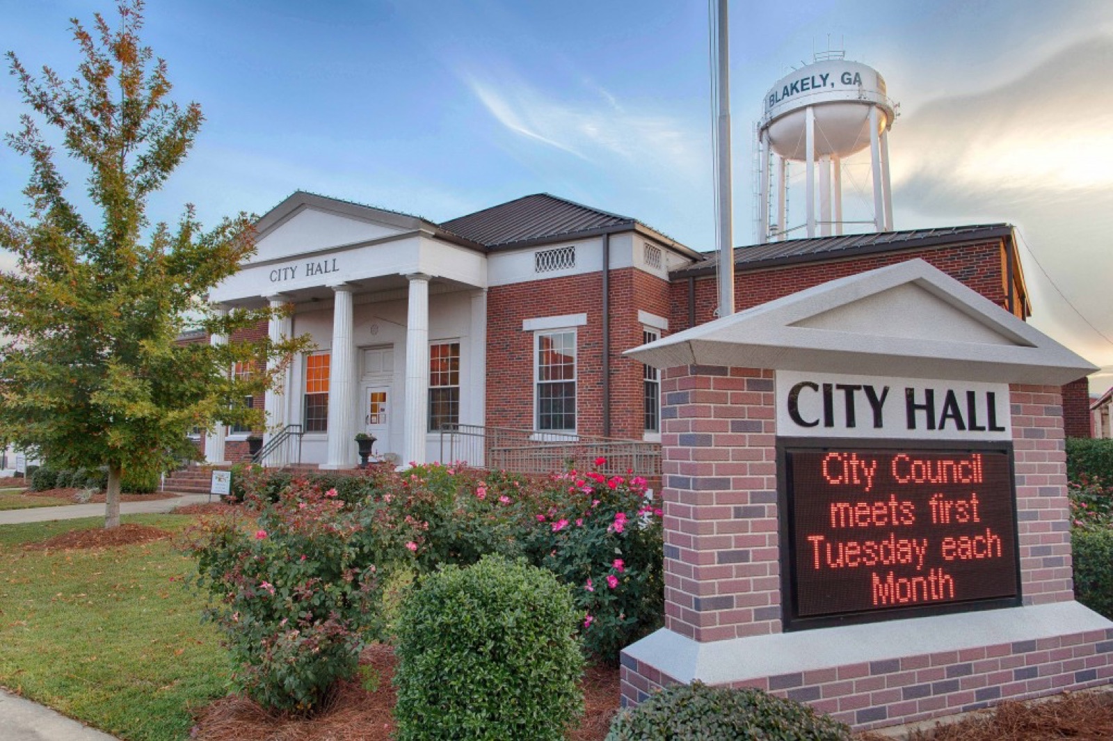 Blakely City Hall, a brick building with white columns, with the Blakely water tower behind it and a sign reading City Council meets first Tuesday each month