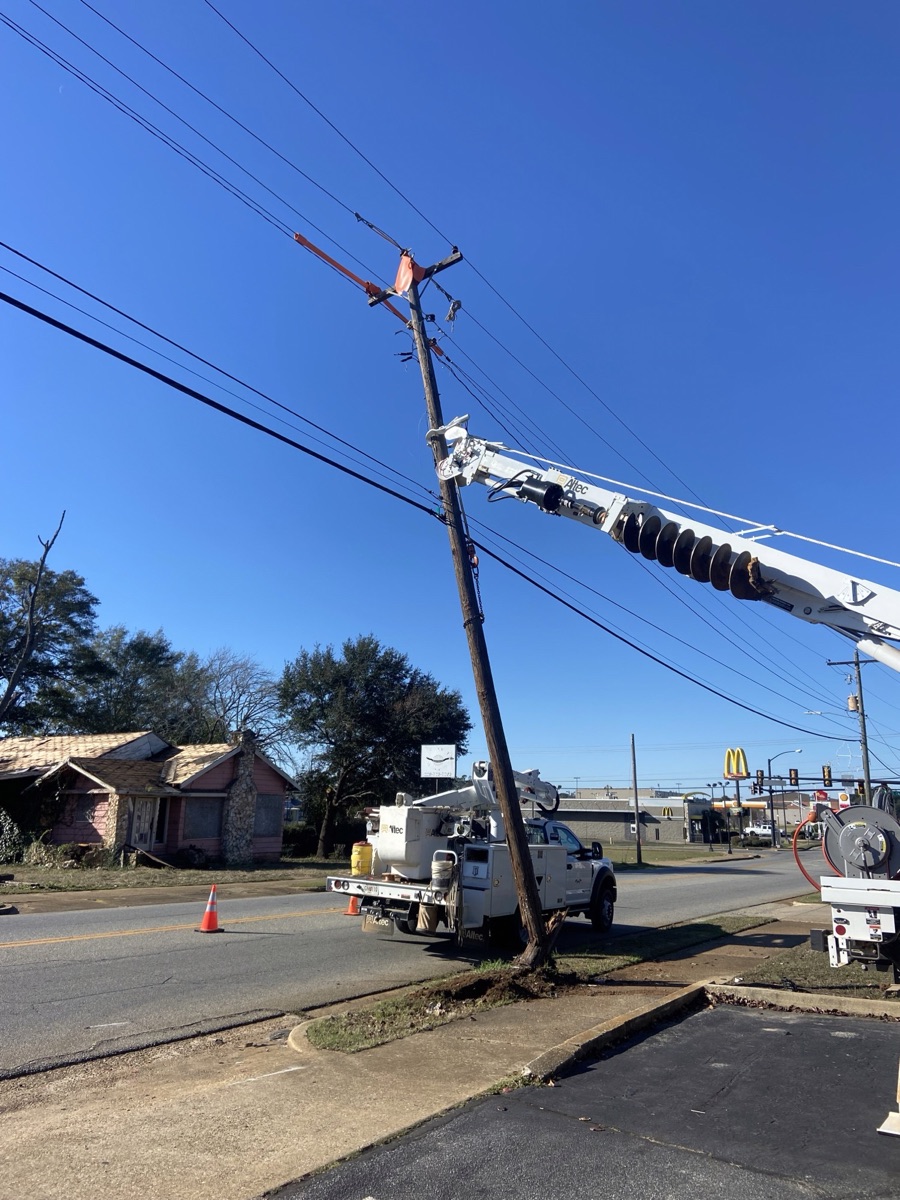The broken pole leaning over Columbia Highway, held by a bucket truck's boom, with traffic cones on the road